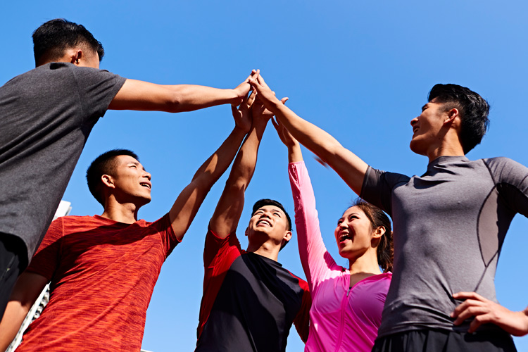 A group of five friends celebrating victory with high-fives against a clear blue sky.